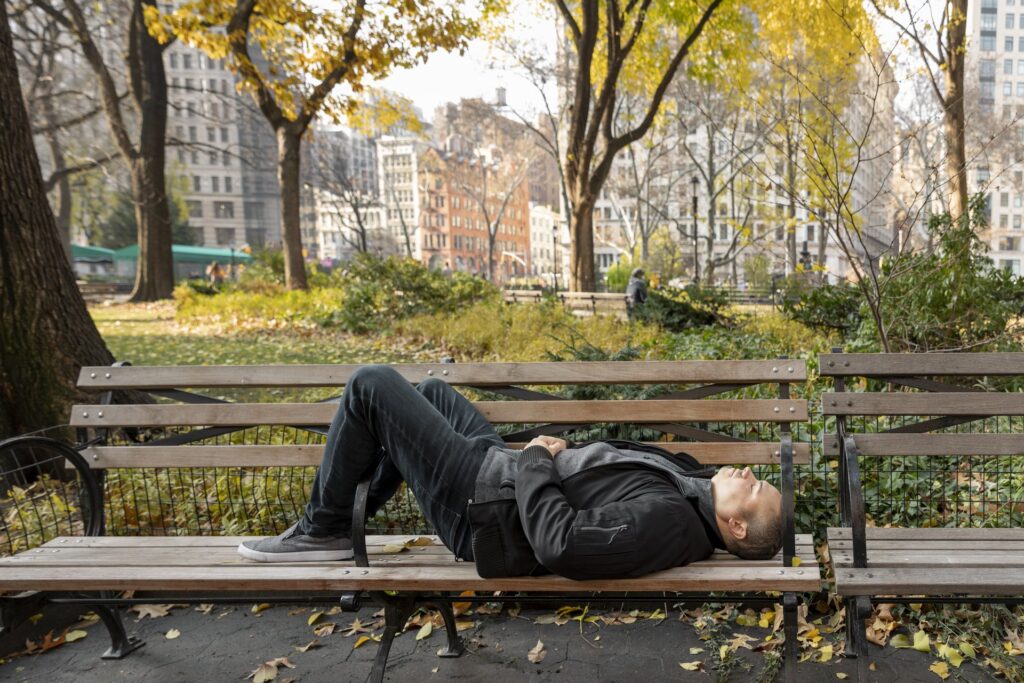 Hombre descansando tumbado en un banco de un parque de Madrid después de caminar.